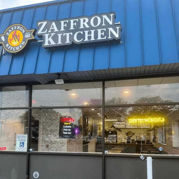 Exterior of Zaffron Kitchen restaurant with a blue awning and large windows showing the interior.