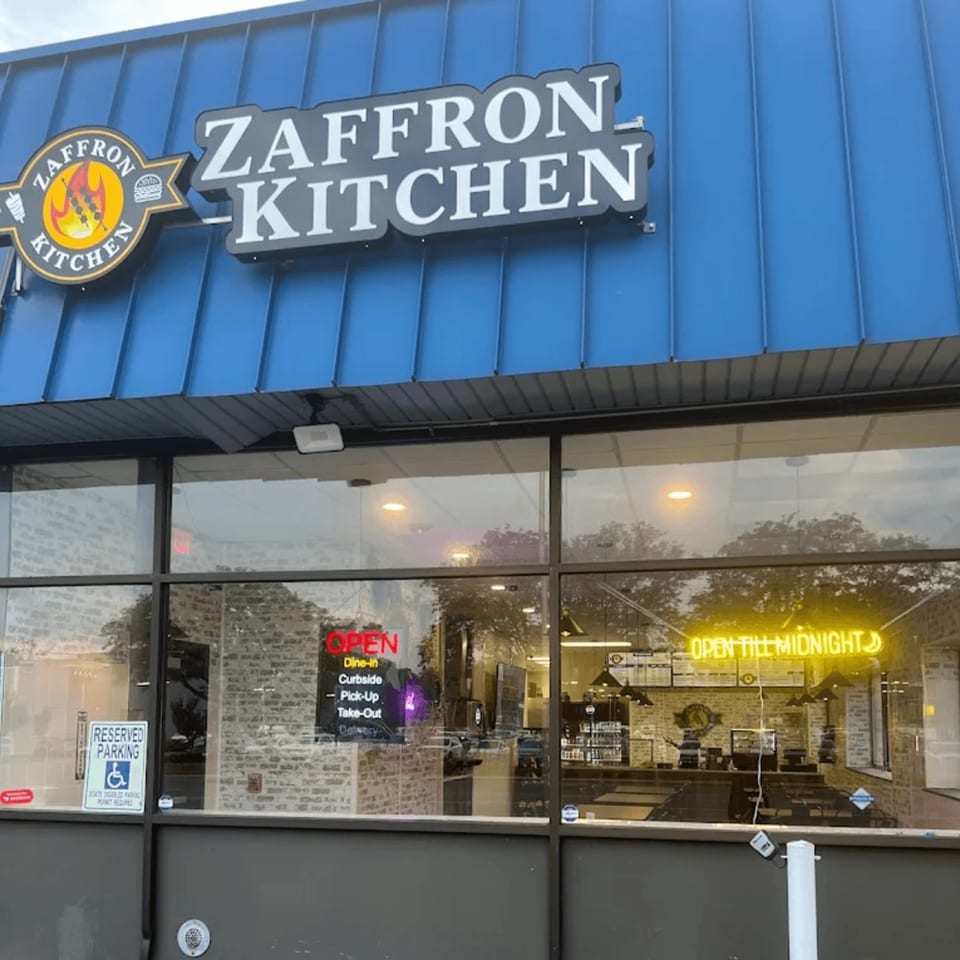 Exterior of Zaffron Kitchen restaurant with a blue awning and large windows showing the interior.