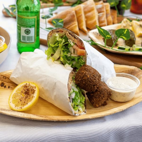 Falafel wrap, falafel balls, and dipping sauce on a wooden plate with a lemon slice.