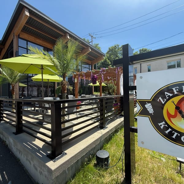 Zaffro Kitchen's outdoor patio with green umbrellas, palm trees, and a wooden pergola.