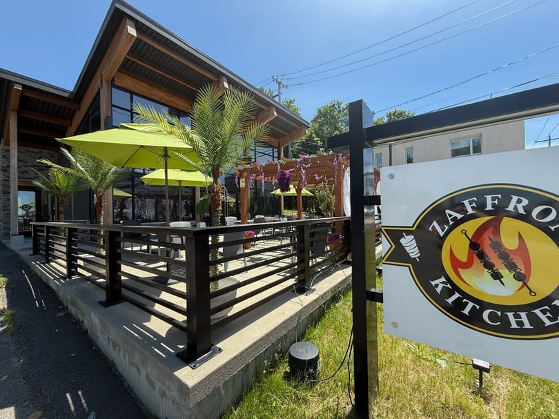 Zaffro Kitchen's outdoor patio with green umbrellas, palm trees, and a wooden pergola.