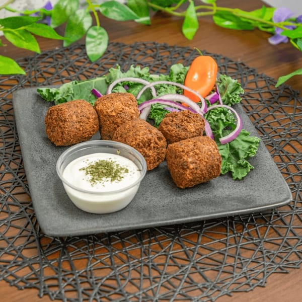 Crispy falafel pieces, fresh kale, red onion, and an orange pepper on a dark plate with sauce.
