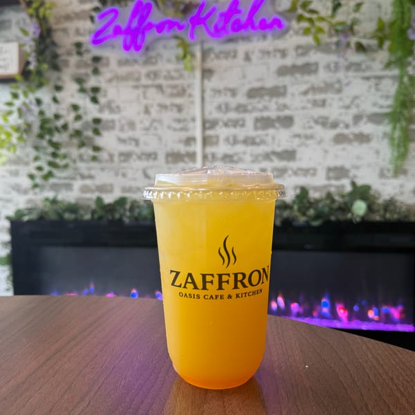 A Zaffron Oasis Cafe & Kitchen branded drink on a table with a neon sign and fireplace.
