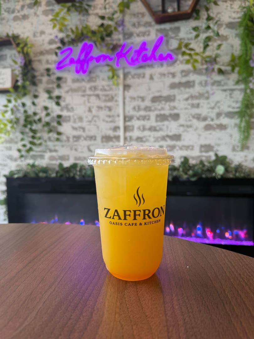 A Zaffron Oasis Cafe & Kitchen branded drink on a table with a neon sign and fireplace.