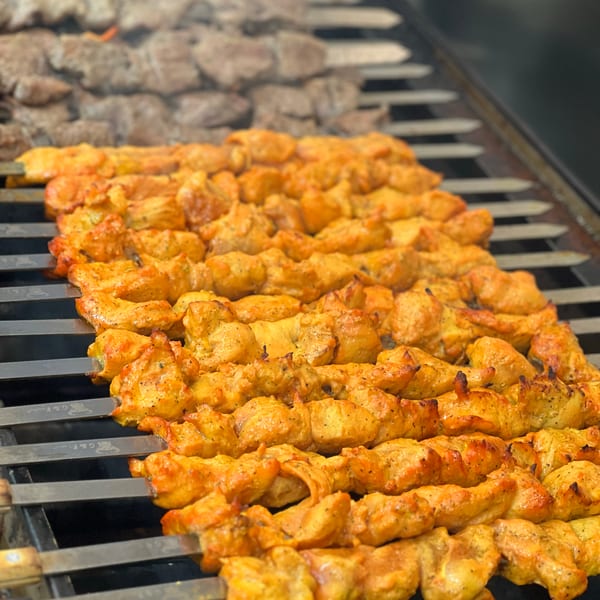 Chicken and beef kebabs cooking on a grill over flames, with smoke rising.