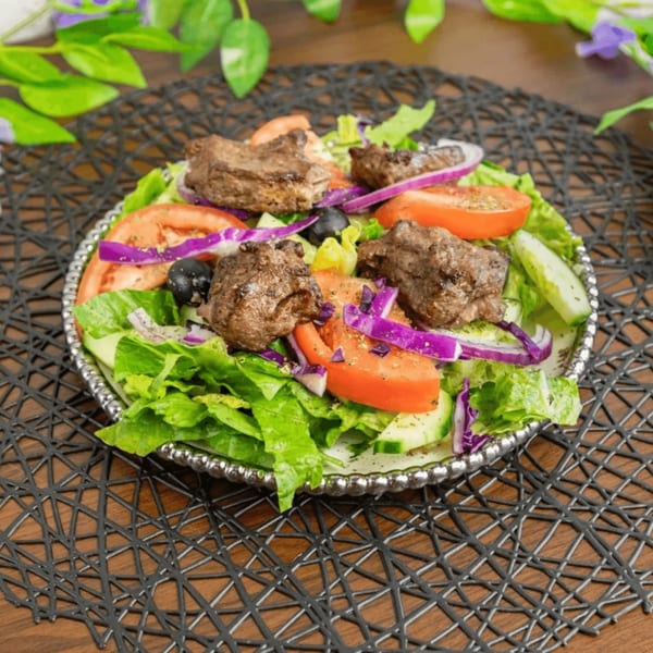Grilled meat chunks on a fresh salad with lettuce, tomatoes, cucumbers, red onions, and olives.
