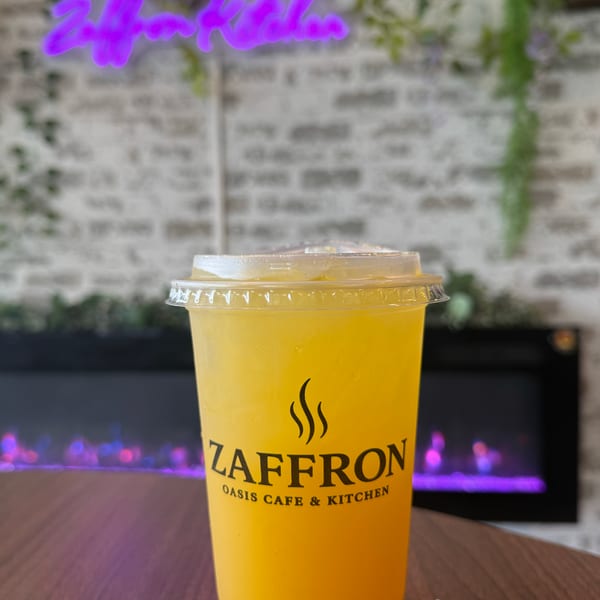 A Zaffron Oasis Cafe & Kitchen branded cup of yellow iced tea on a wooden table.