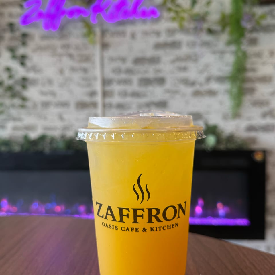 A Zaffron Oasis Cafe & Kitchen branded cup of yellow iced tea on a wooden table.