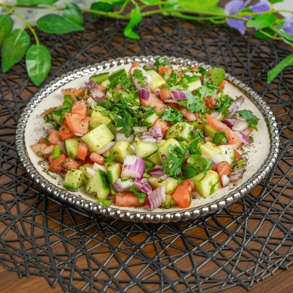 Freshly chopped salad with cucumbers, tomatoes, red onions, and cilantro on a decorative white plate.
