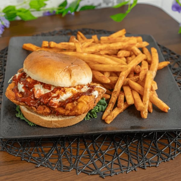 Crispy chicken sandwich with coleslaw and BBQ sauce, served with a side of golden fries.