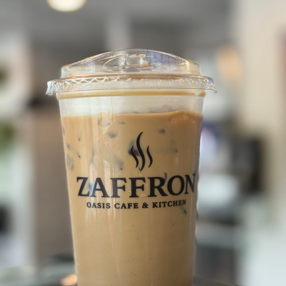 Iced coffee with cream and the Zaffron Oasis Cafe & Kitchen logo on a dark surface.