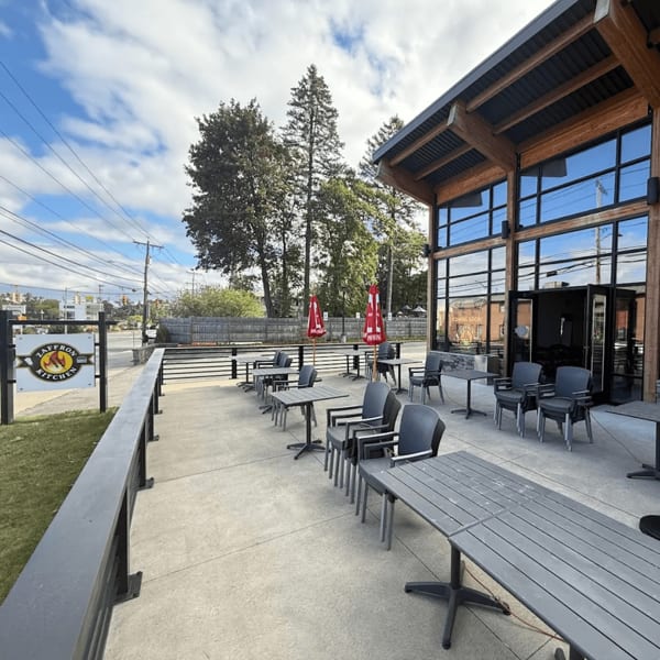 Outdoor patio of Zaffron Kitchen with gray tables and chairs, red umbrellas, and a modern building.