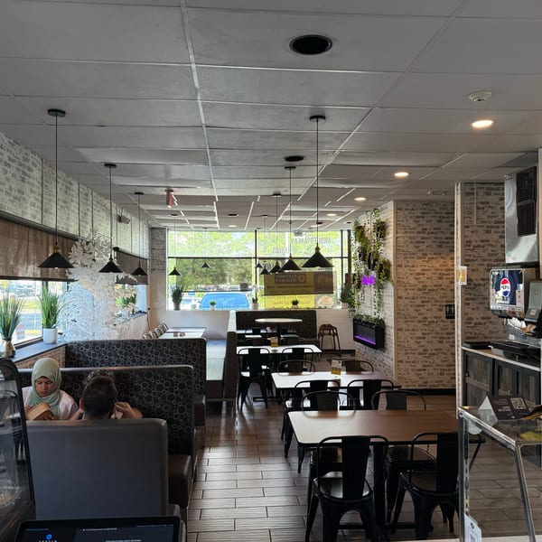 A restaurant interior with brick walls, black tables, and booths, with a few patrons seated.
