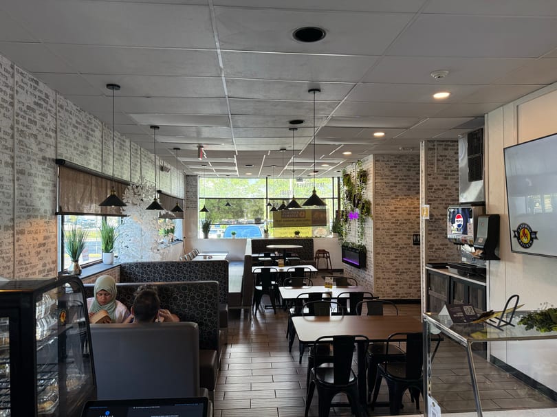A restaurant interior with brick walls, black tables, and booths, with a few patrons seated.