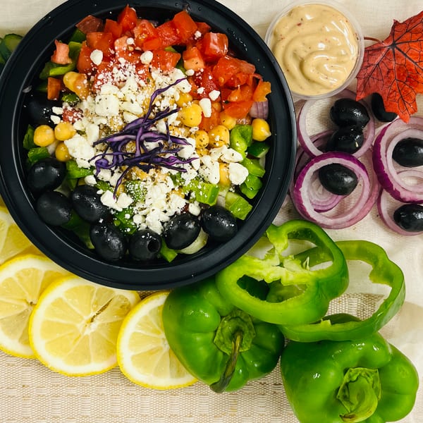 Colorful salad with tomatoes, chickpeas, feta, olives, and red cabbage, surrounded by fresh vegetables.