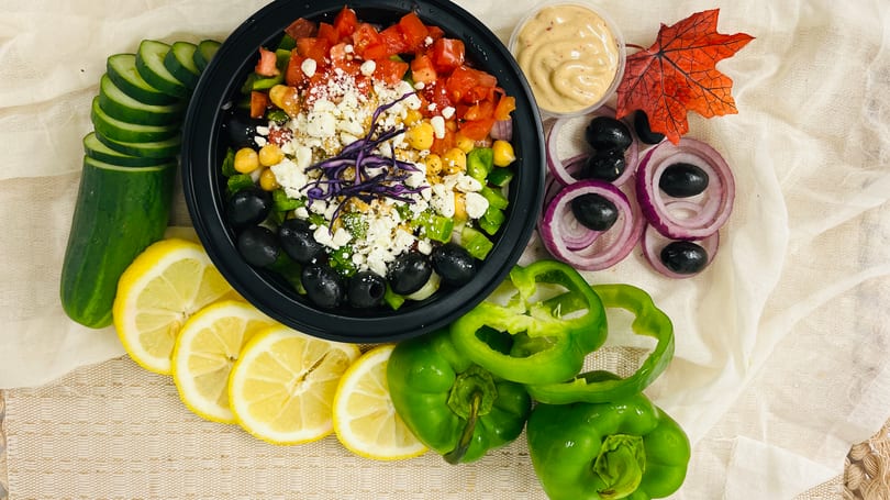 Colorful salad with tomatoes, chickpeas, feta, olives, and red cabbage, surrounded by fresh vegetables.