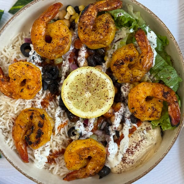Overhead view of a shrimp bowl with rice, hummus, lettuce, olives, and a lemon slice.