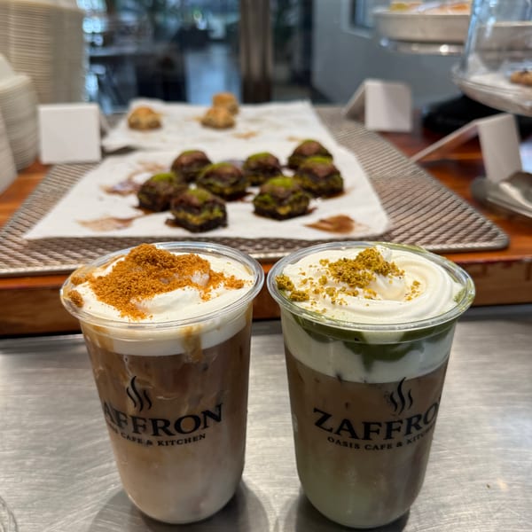 Two iced coffees with whipped cream and toppings, with pastries in the background at Zaffro Oasis Cafe.