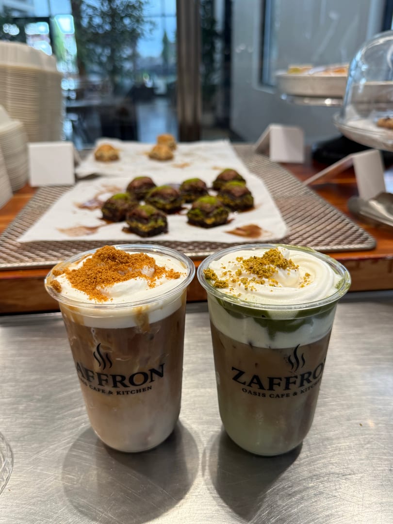 Two iced coffees with whipped cream and toppings, with pastries in the background at Zaffro Oasis Cafe.