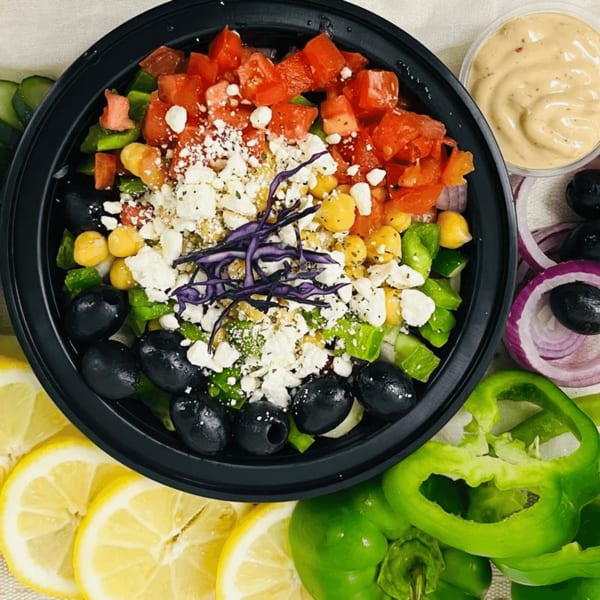 Colorful salad with tomatoes, chickpeas, feta, olives, and red cabbage, surrounded by fresh ingredients.