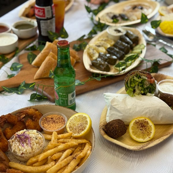 A table laden with various Middle Eastern dishes, including falafel wraps, dolmas, and fried shrimp.