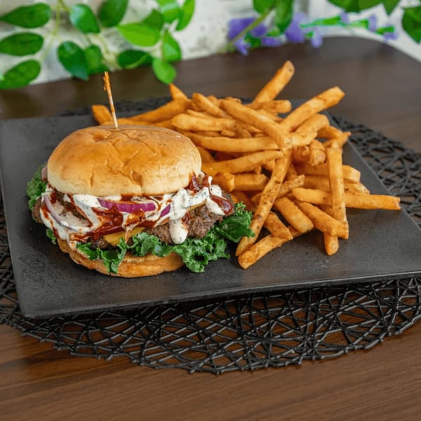 A gourmet burger with red onions, sauce, and lettuce, served with golden french fries on a black plate.