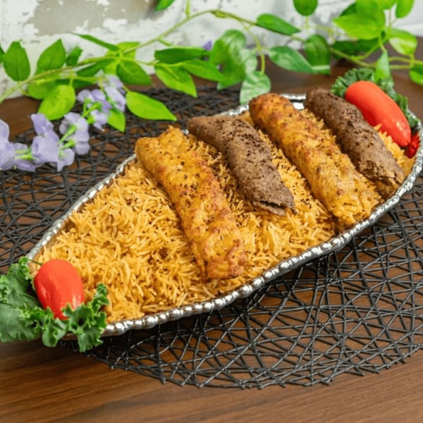 A silver platter of spiced rice with alternating chicken and beef kabobs, garnished with peppers and kale.